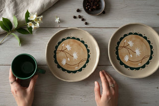 Two ceramic plates with floral designs on a wooden table with a cup and hands holding it.